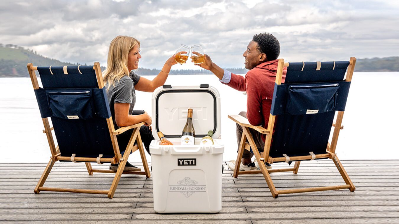 Two people on a dock cheers Kendall-Jackson wine with a Kendall-Jackson logoed Yeti cooler.